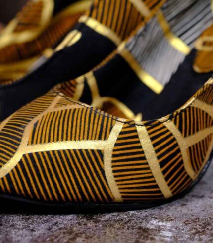 Handmade African Kivu Heels with black, gold, and white geometric patterns, placed on wood and stone background.