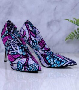 Handmade African Zuba Heels with abstract purple, blue, and black patterns, placed beside a drum and plant on a marble-like surface.