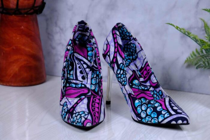 Handmade African Zuba Heels with abstract purple, blue, and black patterns, placed beside a drum and plant on a marble-like surface.