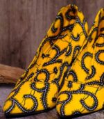 Handmade yellow and black swirl high-heeled shoes on a textured surface.