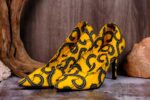 Handmade yellow and black swirl high-heeled shoes on a textured surface.