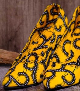 Handmade yellow and black swirl high-heeled shoes on a textured surface.