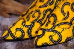 Handmade yellow and black swirl high-heeled shoes on a textured surface.