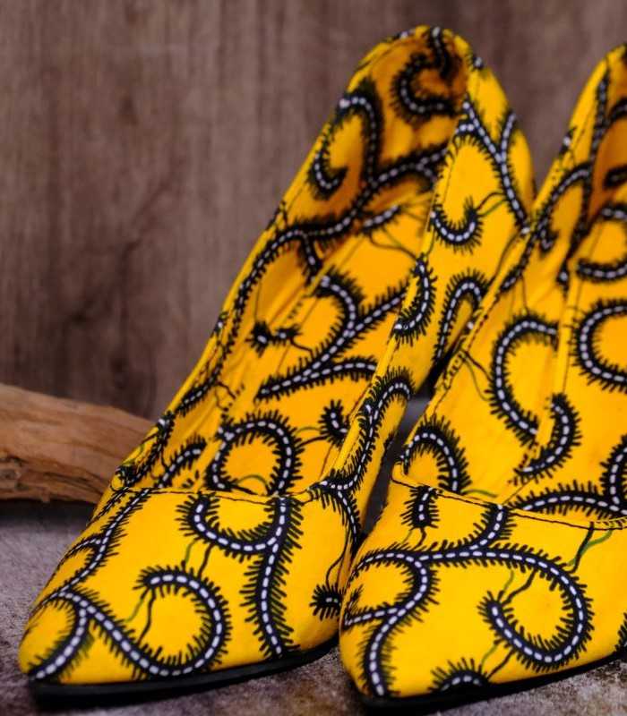 Luma Swirl – Handmade African Print Heels opt Handmade yellow and black swirl high-heeled shoes on a textured surface.
