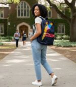 GeoFusion Ankara Backpack with geometric patchwork in burgundy, teal, rose pink, and golden yellow on indigo denim, featuring L’Africaine Boutique logo.