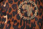 Leopard Luxe Backpack with golden brown and black leopard print, sleek silhouette, front pocket, and L’Africaine Boutique emblem.