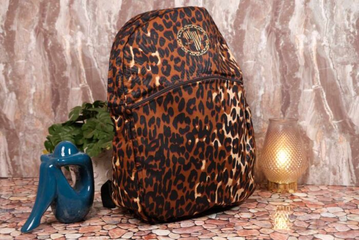Leopard Luxe Backpack with golden brown and black leopard print, sleek silhouette, front pocket, and L’Africaine Boutique emblem.