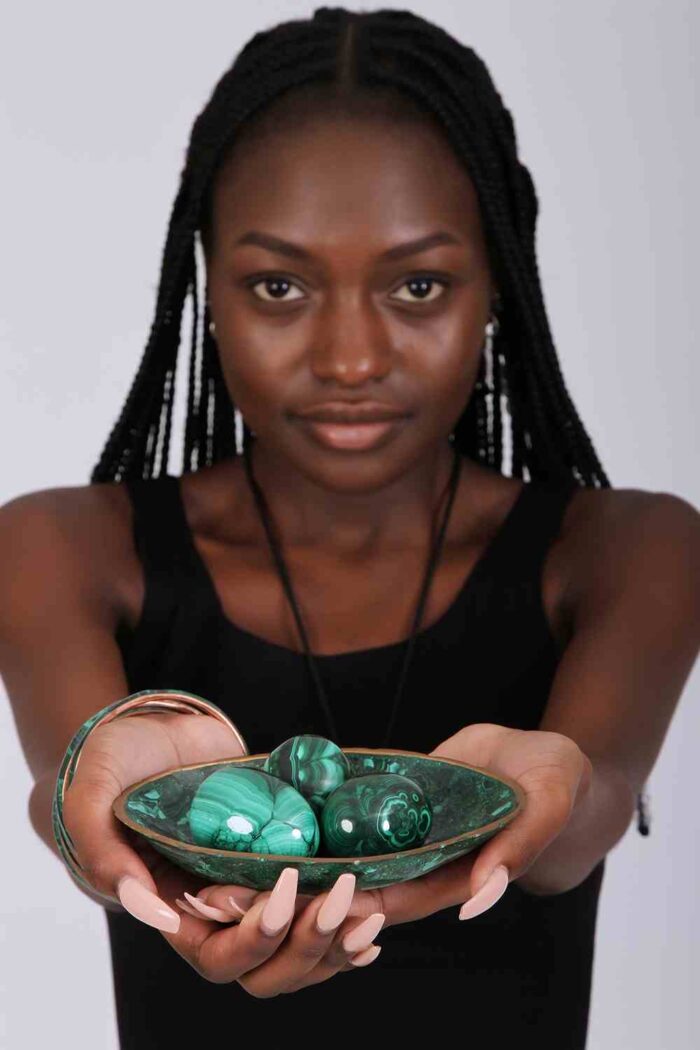 Three polished green malachite spheres in a matching decorative bowl, showcasing natural banding and elegant symmetry.
