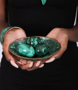 Three polished green malachite spheres in a matching decorative bowl, showcasing natural banding and elegant symmetry.