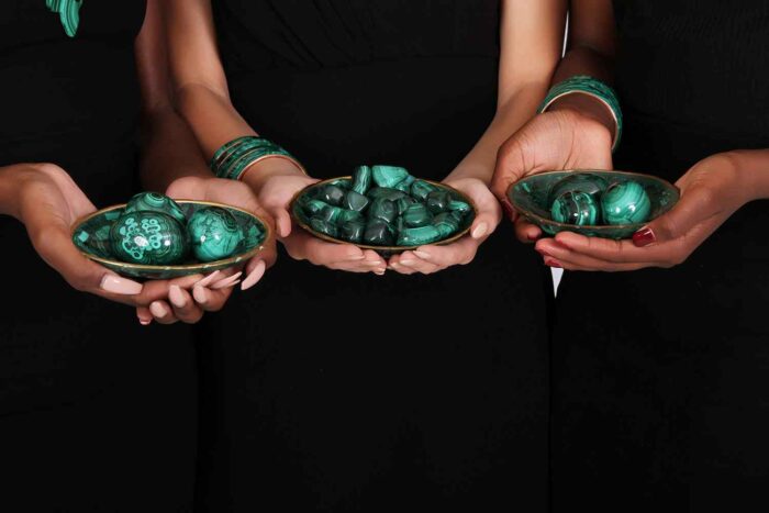 Three polished green malachite spheres in a matching decorative bowl, showcasing natural banding and elegant symmetry.