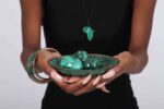 Three polished green malachite spheres in a matching decorative bowl, showcasing natural banding and elegant symmetry.