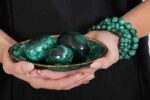 Three polished green malachite spheres in a matching decorative bowl, showcasing natural banding and elegant symmetry.