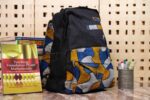 Midnight Geometry Ankara Backpack with black denim and geometric patterns in cobalt blue, golden yellow, and ivory, featuring L’Africaine Boutique logo.