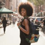 Plume Ankara Backpack with elongated teardrop motifs in teal, golden yellow, and amber orange on ivory, featuring L’Africaine Boutique logo.