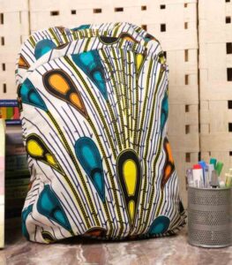 Plume Ankara Backpack with feather-inspired teardrop motifs in teal, golden yellow, and amber orange on ivory base, featuring L’Africaine Boutique logo.