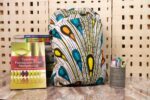 Plume Ankara Backpack with feather-inspired teardrop motifs in teal, golden yellow, and amber orange on ivory base, featuring L’Africaine Boutique logo.