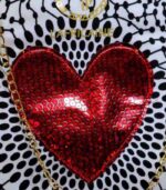 Red Heart Statement Bag with black and white patterned fabric, red sequined heart, and gold chain handles. Displayed against a stone wall with rocks.