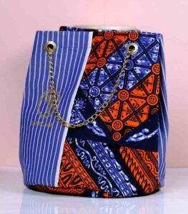 Sanaa African Cinch Bag made from Ankara fabric with blue pinstripes, orange and navy “L’Africaine” motif, and gold chain strap.