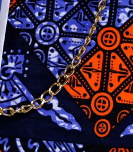 Sanaa African Cinch Bag made from Ankara fabric with blue pinstripes, orange and navy “L’Africaine” motif, and gold chain strap.