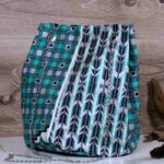 Teal Geometry Cinch Bag with teal, black, and white geometric print, silver chain strap, and drawstring closure. Displayed with plant and driftwood decor.