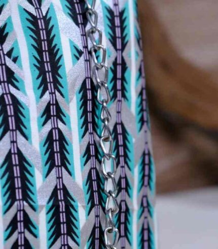 Teal Geometry Cinch Bag with teal, black, and white geometric print, silver chain strap, and drawstring closure. Displayed with plant and driftwood decor.