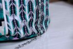 Teal Geometry Cinch Bag with teal, black, and white geometric print, silver chain strap, and drawstring closure. Displayed with plant and driftwood decor.