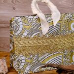 The Terra Tote Bag made from Ankara fabric with gold and white swirl design, golden embroidery, and padded cream handles.
