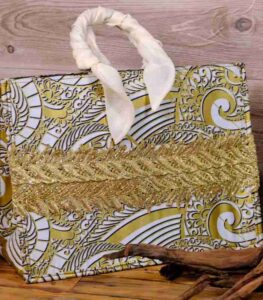 The Terra Tote Bag made from Ankara fabric with gold and white swirl design, golden embroidery, and padded cream handles.