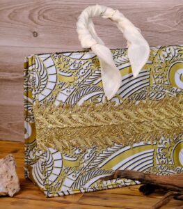 The Terra Tote Bag made from Ankara fabric with gold and white swirl design, golden embroidery, and padded cream handles.