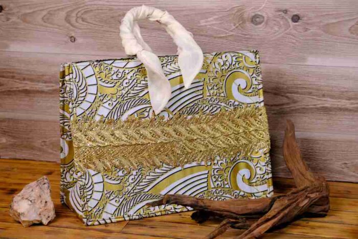 The Terra Tote Bag made from Ankara fabric with gold and white swirl design, golden embroidery, and padded cream handles.
