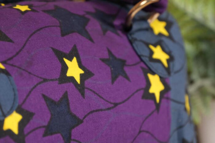 ankara star print handbag in deep purple and navy Ankara wax fabric with bold yellow and black star patterns, gold rings, and top zipper closure.