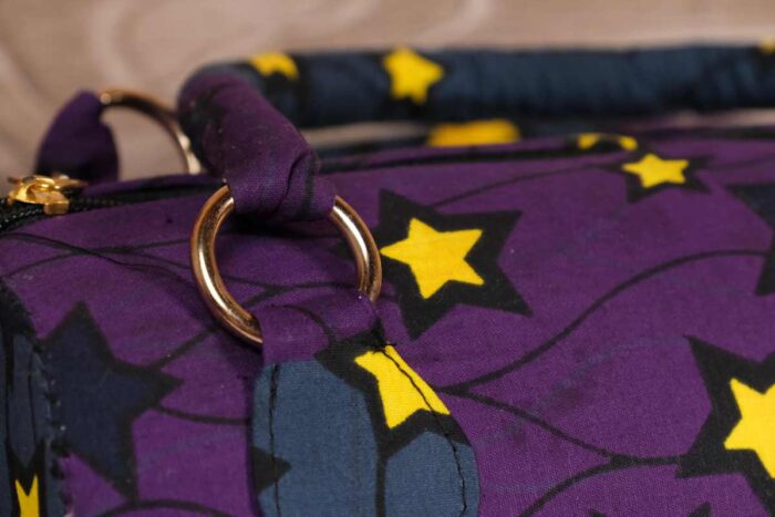 ankara star print handbag in deep purple and navy Ankara wax fabric with bold yellow and black star patterns, gold rings, and top zipper closure.