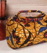Mustard Ankara handbag in wax fabric with navy, red, and black floral and leaf patterns, padded handles, and gold zip closure.