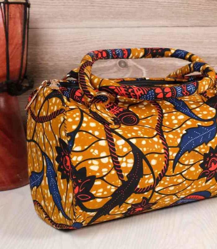 Mustard Ankara handbag 2 Mustard Ankara handbag in wax fabric with navy, red, and black floral and leaf patterns, padded handles, and gold zip closure.