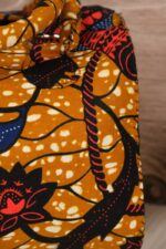 Mustard Ankara handbag in wax fabric with navy, red, and black floral and leaf patterns, padded handles, and gold zip closure.