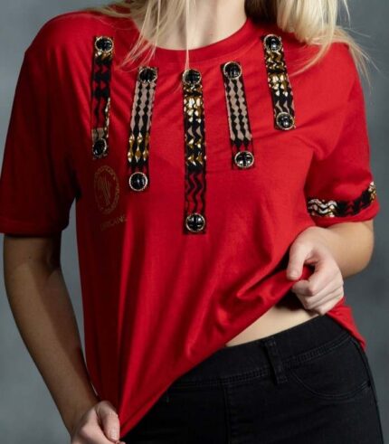 Red tee with vertical black and gold patterned strips and circular embellishments on chest and sleeves from L’Africaine Boutique.
