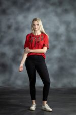 Red tee with vertical black and gold patterned strips and circular embellishments on chest and sleeves from L’Africaine Boutique.