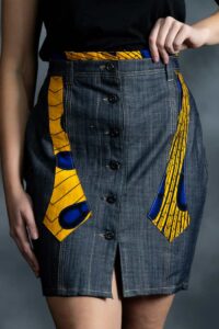 Slim grey-blue denim skirt with asymmetric button closure and muted Ankara accents on waistband and pockets.