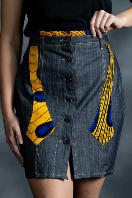 Slim grey-blue denim skirt with asymmetric button closure and muted Ankara accents on waistband and pockets.