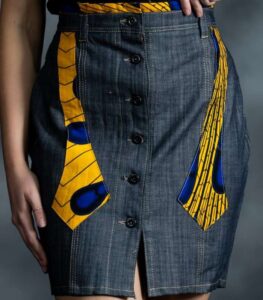 Slim grey-blue denim skirt with asymmetric button closure and muted Ankara accents on waistband and pockets.