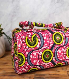 ankara circular pattern handbag in vibrant pink wax fabric with yellow, green, and navy circular motifs accented by white speckles, padded handles, and gold rings.