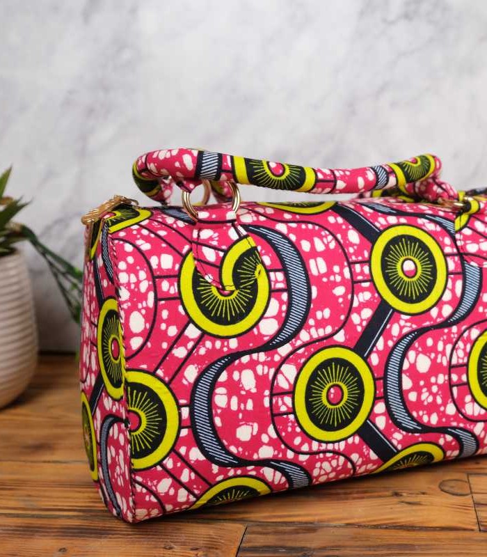 Ankara circular pattern handbag 8 ankara circular pattern handbag in vibrant pink wax fabric with yellow, green, and navy circular motifs accented by white speckles, padded handles, and gold rings.