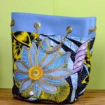 ankara embroidered flower bucket by L’Africaine Boutique—crafted from wax fabric with oversized embroidered flower, gold chain strap, and faux leather trim.