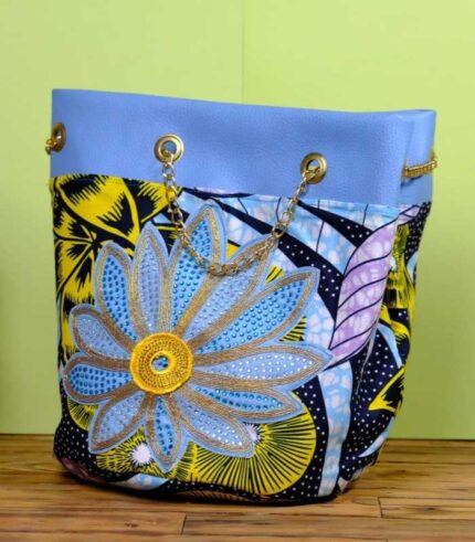 ankara embroidered flower bucket by L’Africaine Boutique—crafted from wax fabric with oversized embroidered flower, gold chain strap, and faux leather trim.