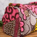 ankara floral swirl handbag in vibrant pink wax fabric with yellow, white, and brown floral swirl patterns, padded handles, gold rings, and top zipper.