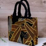 ankara golden noir handbag in black and golden-brown Ankara wax fabric with feather-like motifs, padded black handles, structured silhouette, and handcrafted front accent.