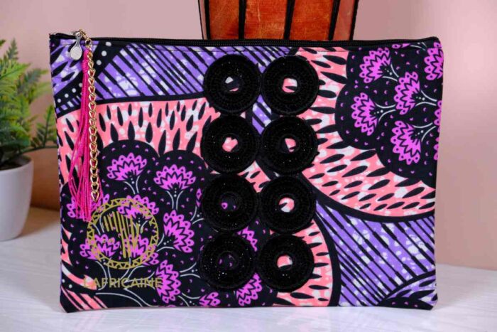 ankara midnight bloom clutch in purple, pink, and black Ankara wax fabric with hand-embroidered sequin rings, gold logo, and pink tassel zipper accent.