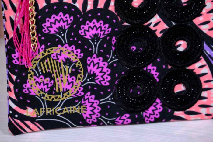 ankara midnight bloom clutch in purple, pink, and black Ankara wax fabric with hand-embroidered sequin rings, gold logo, and pink tassel zipper accent.