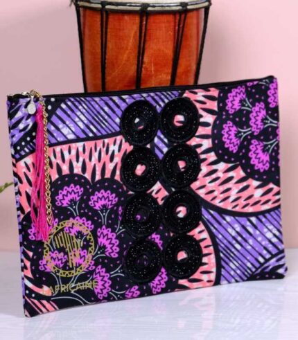 ankara midnight bloom clutch in purple, pink, and black Ankara wax fabric with hand-embroidered sequin rings, gold logo, and pink tassel zipper accent.