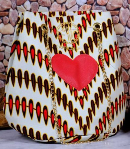 ankara red heart bucket in white, red, and black Ankara wax fabric with bold red heart accent, gold chain strap, and structured bucket silhouette.